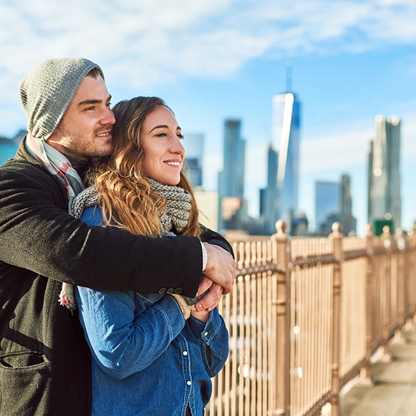 Una pareja abrazada en un puente y de fondo Nueva York.