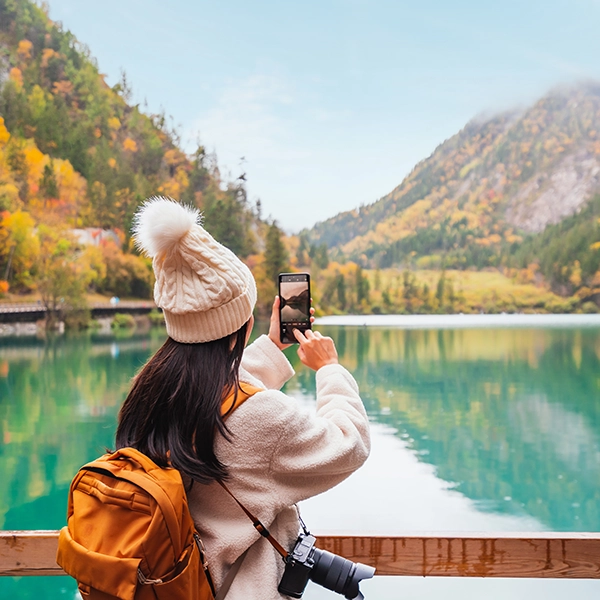 Una turista haciendo foto del paisaje donde se ve un lago y las montañas.